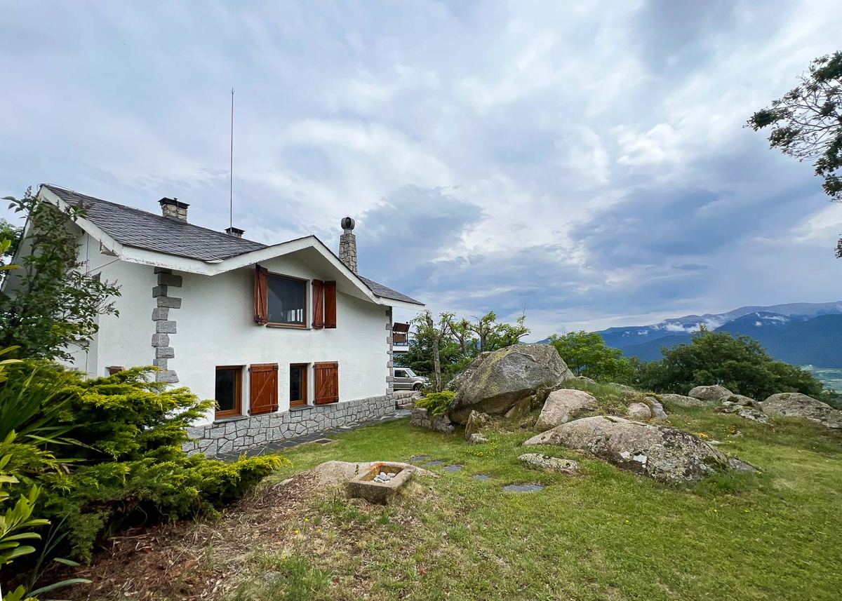 La casa blanca con el jardín de rocas de granito y el Cadí al fondo